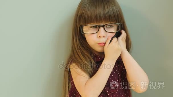 可爱的小女孩，戴着大眼镜移动电话交谈。关闭。灰色背景