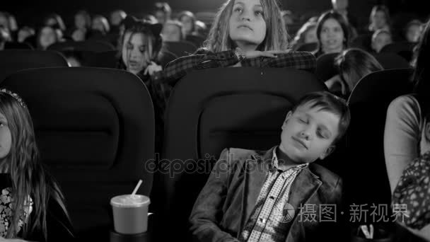黑色和白色的镜头。昏昏欲睡的男孩害怕在电影院。孩子们看着大屏幕上的卡通
