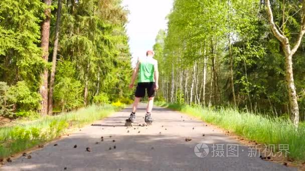 在绿色的运行态内联滑冰的后视。在森林里顺利沥青延度的室外轮滑。浅色皮肤的男人一脚踏入松果的道路上，与重心移动