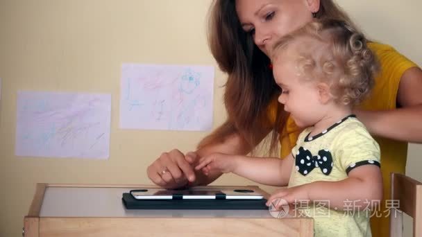 母亲帮她使用平板电脑坐在桌旁的小女孩