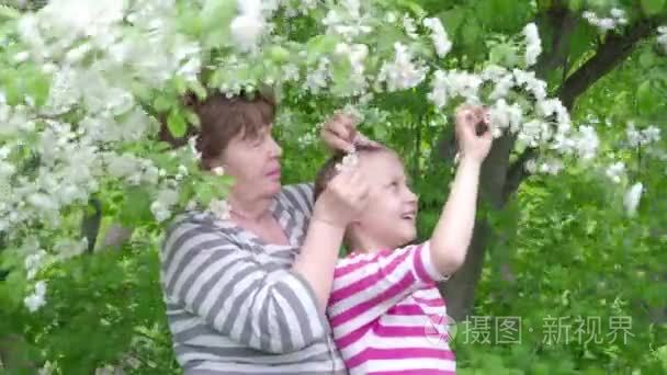 快乐的老年妇女和女孩在公园里盛开的苹果树之间。4 k视频