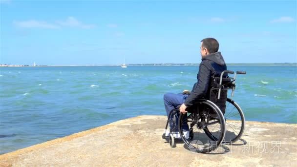 禁用年轻男子坐在轮椅上，看着大海