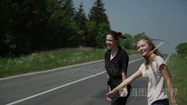 两个年轻女性旅行者站在旁边和要求停止过往的汽车
