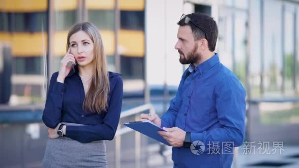 商务女士和她的助手交谈在手机上一个大的投资者，在大街上，男人在文档中做笔记