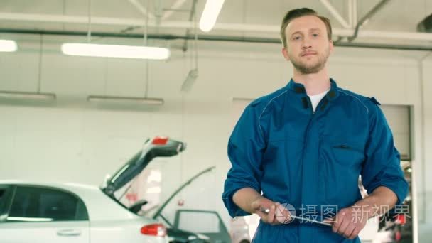 严重的白种人年轻汽车机械人在维修服务背景的手里拿着一把扳手同时构成手的蓝色制服。室内