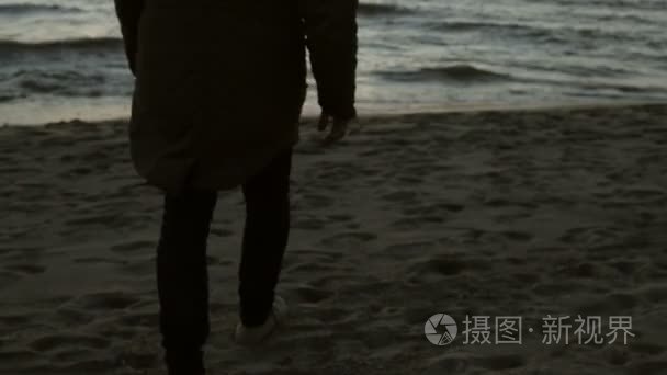 孤独的人走在海岸上的大海和欣赏落日美景。年轻男性钦佩在海滩上波