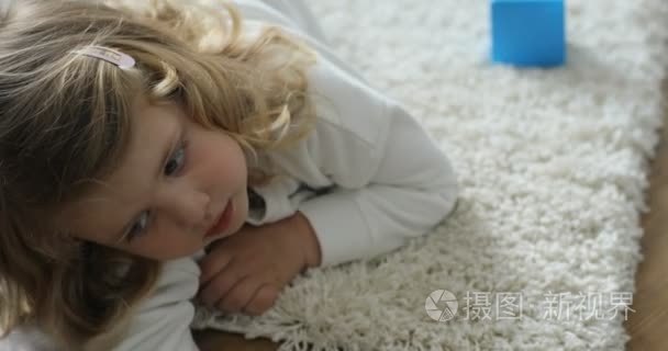 在家里的地板上躺在一天时间的金发卷曲的头发的小女孩的画像。室内视频