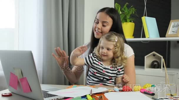 长长的黑发和卷曲的金发视频聊与家庭背景的笔记本电脑上的父亲和她女儿的年轻女子