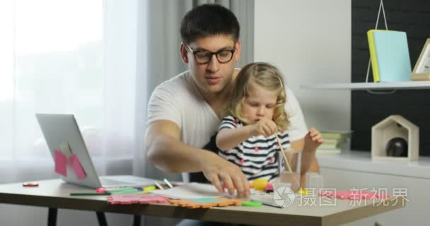 白种人金黄色卷发用颜料绘制在一张纸选址与她的父亲在家里的小女孩