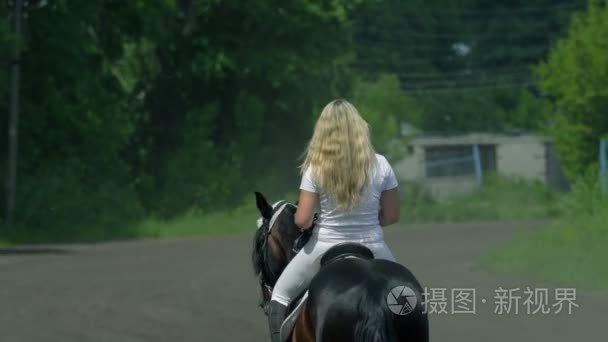 一个漂亮的女孩，在白色的头发和白色的衣服，慢慢地骑黑色棕色骏马飞驰。这个女孩完成培训，到娱乐场所去。女孩是有点累了，是可见她脸上
