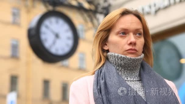一个女人在一件粉红色的外套和毛衣是站在拥挤的街道，时钟附近，等待会议