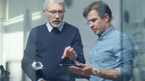 平板电脑在讨论技术细节的两个高级工程师。两人看起来体面和专业。办公室是现代的光明