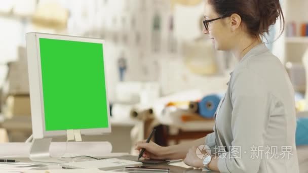 美丽的时装设计师坐在她的办公桌前与绿色屏幕，使用数字绘图平板个人电脑。她的工作室是阳光，全部的多彩细节 面料 缝纫项目，草图视频