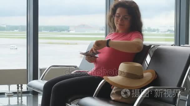 年轻女子在国际机场望着智能手机，等待她的航班