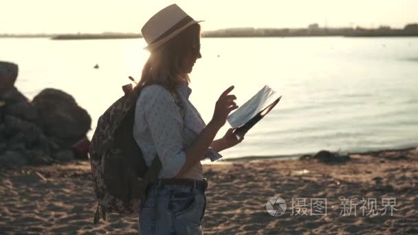 那个女孩是一位游客选择在上的旅游目的地。年轻女人时髦太阳镜和帽子。在日落时在海滩上的女孩