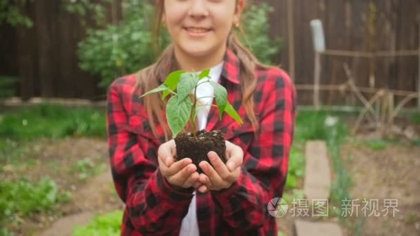 微笑的年轻女子假扮与幼苗在花园的慢动作视频