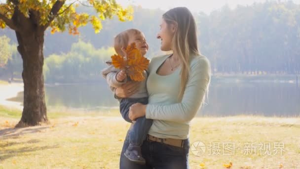 美丽的母亲抱着襁褓中的儿子和摘树叶在秋天公园 4 k 特写镜头
