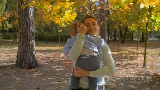 美丽充满爱心的母亲，拥抱她的宝贝儿子在秋天公园在大树下的慢动作镜头
