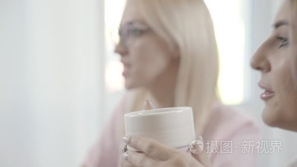 带尖锐特征的年轻女人喝茶，看着共同的患者