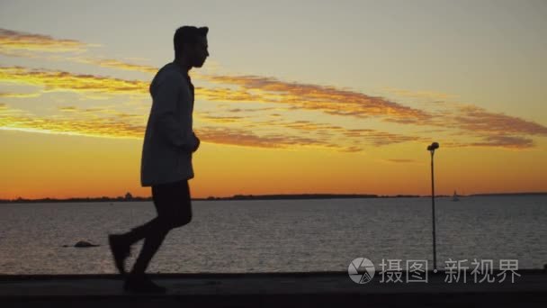 在日落的时候沿着海岸慢跑的男人