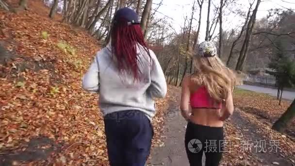 后面的观点的两个有吸引力的多元文化女友早上慢跑。公园位置
