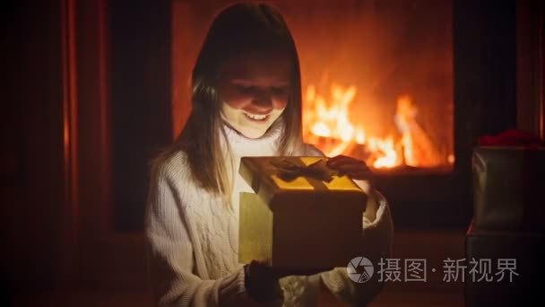 激动的女孩偷看圣诞礼品盒的画像。魔尘和发光灯飞出的打开框