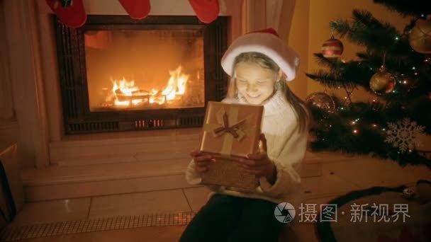 肖像的快乐兴奋的女孩坐在壁炉旁打开圣诞礼品盒