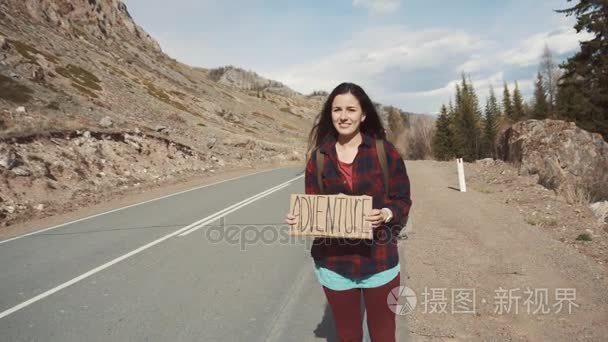 十几岁的女孩举冒险牌子上山路、 微笑和大笑。搭便车去历险