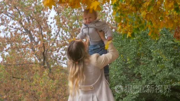 4 的 k 镜头的快乐年轻的母亲抱着和她可爱的宝贝儿子在秋天公园玩