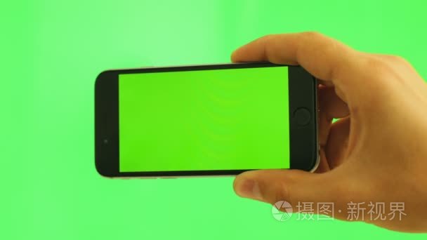 关闭了水平手机与绿屏。男子手持绿色背景上的黑色智能手机与绿屏。色度键