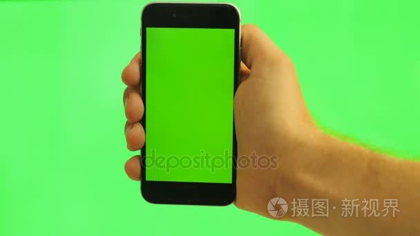 关闭了垂直手机与绿屏。男子手持绿色背景上的黑色智能手机与绿屏。色度键
