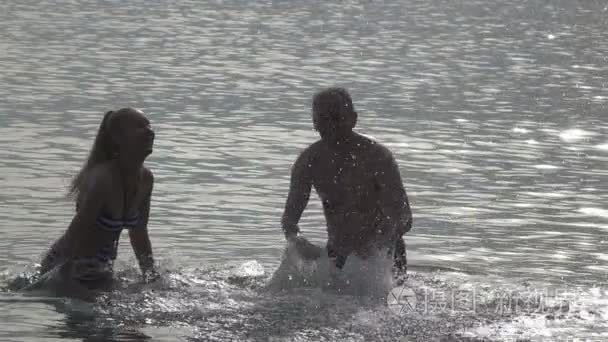 年轻的男人和女人的人，站在海和溅起的水手，慢动作的剪影