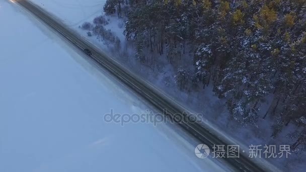 一辆汽车在乡村公路上开车穿过冬季的森林。无人机的顶视图。通过在冬天用雪覆盖了树山高处林区道路鸟瞰图