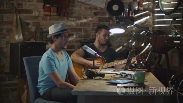 两个年轻人唱歌和弹吉他时在一间车库里的家庭工作室录制一首歌