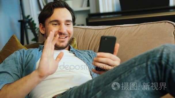 的男人聊天 skype 在家里的沙发上休息时使用智能手机的朋友短视频