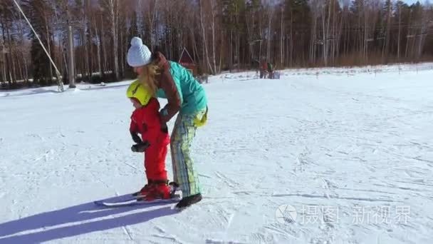 美丽的年轻妈妈帮助小孩滑雪视频