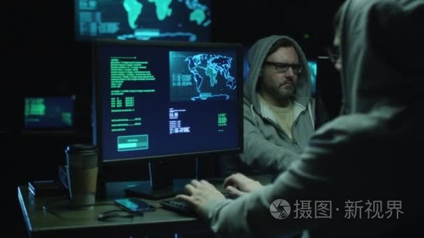 在通风柜中的两个黑客在地图与数据在一个黑暗的办公室房间显示屏幕上的计算机上工作