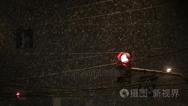 交通灯照耀在降雪期间。恶劣的天气，雨和湿的雪的道路上。思考的夜晚灯光。车头灯