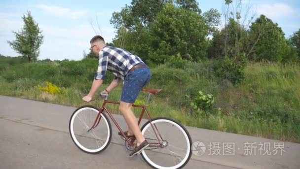 年轻英俊的男人在老式自行车骑在乡间小路上。运动型的家伙在赛道骑自行车。男性单车固定齿轮自行车公路。健康积极的生活方式慢动作