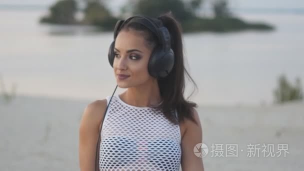 女人戴着耳机听音乐或说话的女孩在使用智能手机快乐的比基尼海滩上使用移动智能手机视频