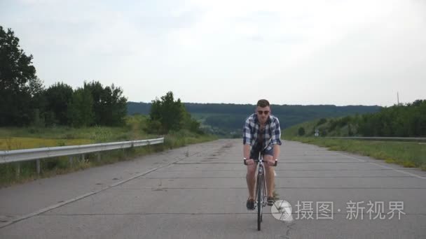 年轻英俊的男人在老式自行车骑在乡间小路上。运动型的家伙在赛道骑自行车。男性单车固定齿轮自行车公路。健康积极的生活方式慢动作前视图