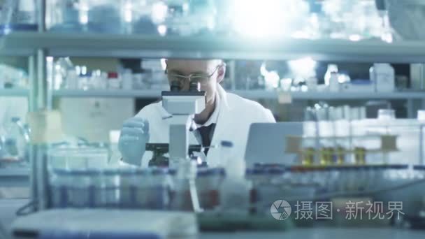 男性的资深科学家是集中用在实验室显微镜工作时