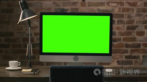绿屏站旁边平板电脑、 灯、 咖啡杯、 笔记本和鼠标在一间阁楼里的桌子上的电脑显示器的画面