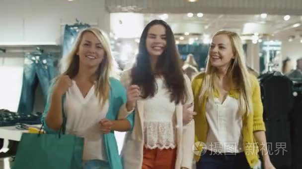 三个快乐的女孩都走过一家服装店在五颜六色的服装