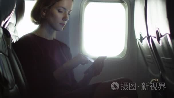 年轻女子使用智能手机内部飞机的窗边