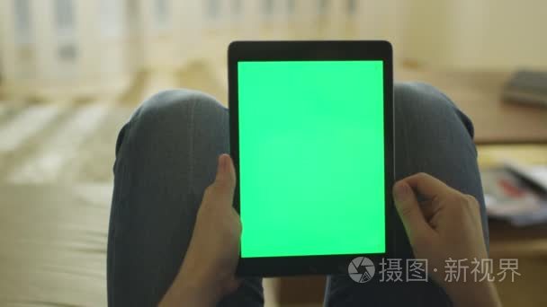 男人是铺设在家里的沙发上和绿色屏幕在肖像模式下在膝上使用平板电脑