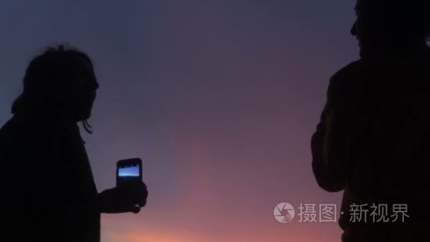 一个男人和女人用色彩斑斓的天空对智能手机的剪影