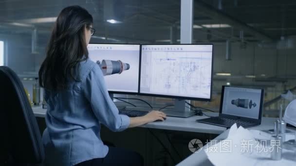 首席女工程师设计的涡轮或发动机零件的三维模型上。第二个监视器显示技术蓝图。从办公室窗口大工厂里见过