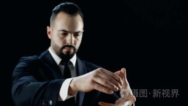 一个专业的魔术师，在黑色西装表演纸牌魔术的特写镜头。引发和捕捉卡甲板在空气中。背景是黑色