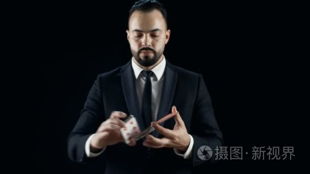 专业魔术师在一套黑色西装执行花招纸牌戏法。背景是黑色